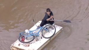 Menino improvisa e transforma porta em canoa para resgatar bicicleta em meio às enchentes no Rio Grande do Sul